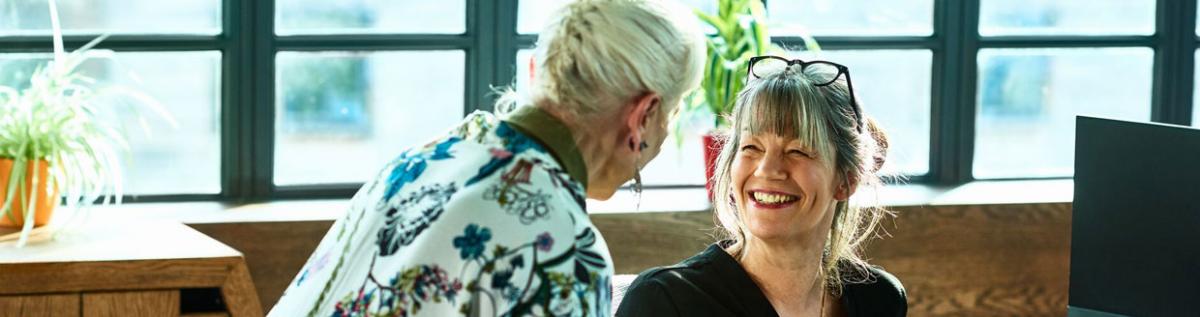 Why Josh Lamb recommends NS&I - the image is of two ladies talking and smiling, the lady facing the camera has her glasses perched stylishly on the top of her hair